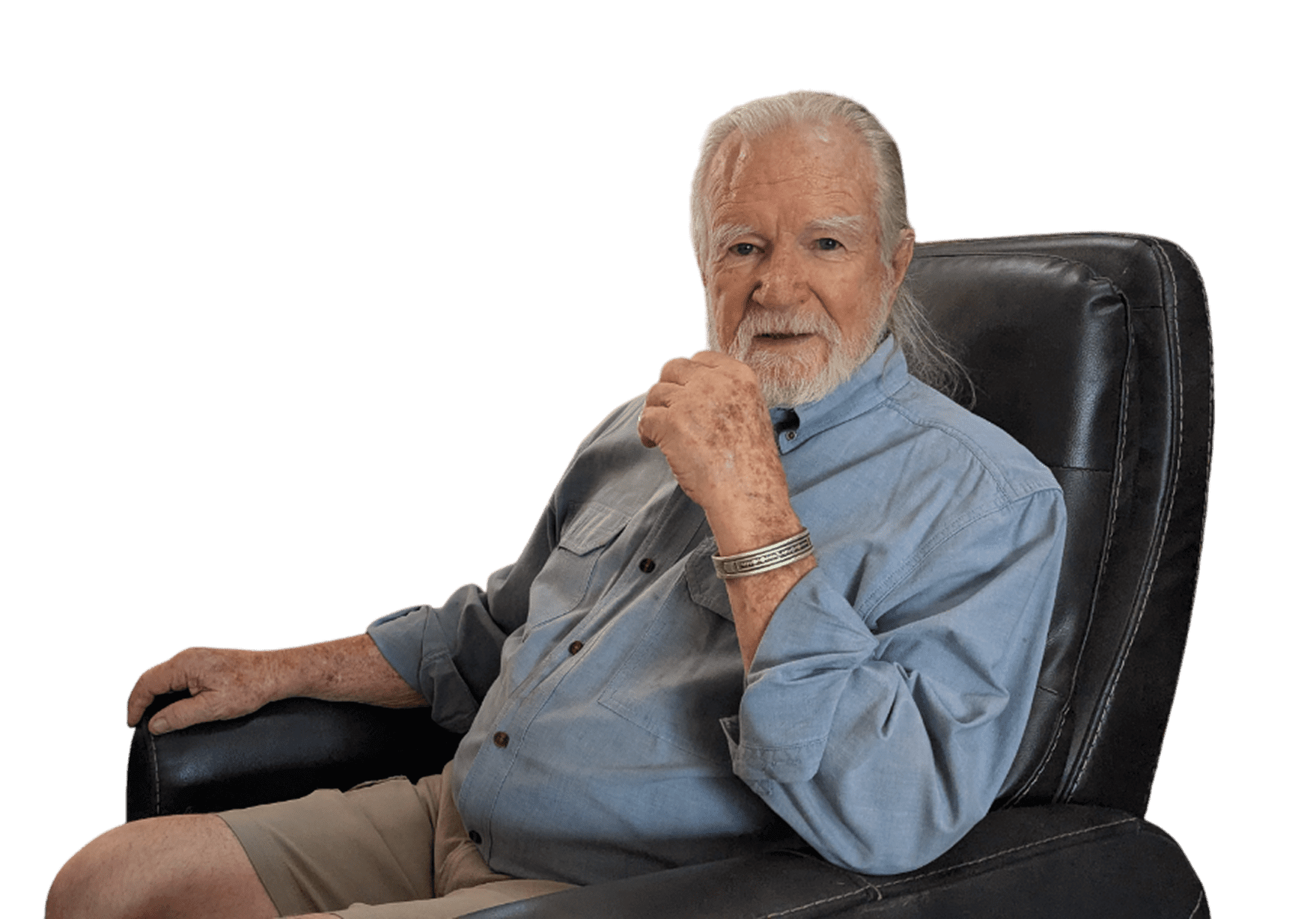 Elderly man sitting thoughtfully in a chair, wearing a denim shirt.